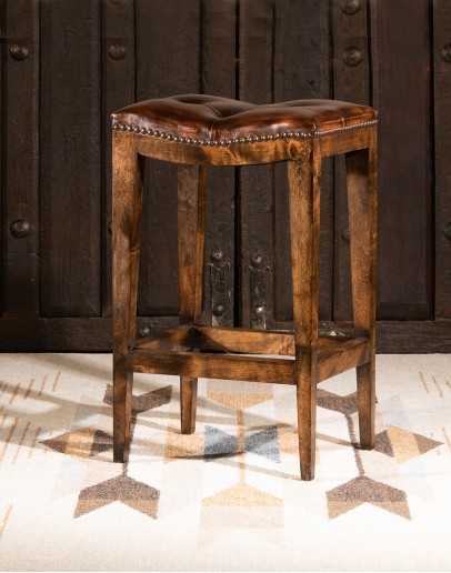 Cheyenne Saddle Stool in top-grain tufted leather with a two-toned color and brass nail heads, on a Knotty Alder hardwood frame with a footrest for added comfort and support. Available in bar and counter height. Backless design saves space