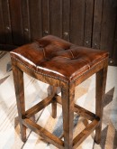 Cheyenne Saddle Stool in top-grain tufted leather with a two-toned color and brass nail heads, on a Knotty Alder hardwood frame with a footrest for added comfort and support. Available in bar and counter height. Backless design saves space