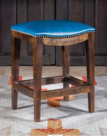 Levi Saddle Stool An image showcasing the Levi Saddle Stool, a masterpiece of American craftsmanship. The stool features a denim blue aniline dyed full grain leather seat, lightly sanded for a distressed look. Its clean-lined design boasts solid Alder Wood straight legs, r
