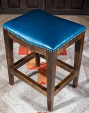 An image showcasing the Levi Saddle Stool, a masterpiece of American craftsmanship. The stool features a denim blue aniline dyed full grain leather seat, lightly sanded for a distressed look. Its clean-lined design boasts solid Alder Wood straight legs, r
