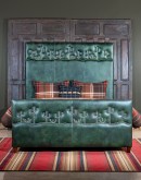 A luxurious green leather upholstered bed, American-made with clean lines and hand burnished details. Features unique nickel nail trim with cactus designs on the headboard and footboard, presenting a tall, art-like stature in the bedroom.