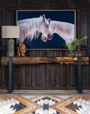 Art piece 'Mirrored Beauty,' depicting two white horses crossing necks against a black background, beautifully framed in light finished wood.