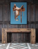 Add rustic charm to your space with this detailed western saddle artwork, set against a serene sky blue background. Framed with a mat back wood frame and coated in a clear semi-gloss epoxy, it ensures vivid colors and lasting protection.