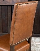 Sundance Saddle Leather Dining Chair featuring solid American Alder Wood frame with black walnut finish, saddle tan leather upholstery, brass nail tacks, and boot stitch emblem.