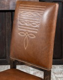 Sundance Saddle Leather Dining Chair featuring solid American Alder Wood frame with black walnut finish, saddle tan leather upholstery, brass nail tacks, and boot stitch emblem.