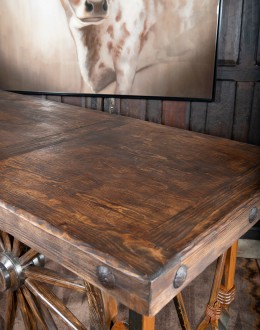 Western-style Pioneer Wagon Wheel Pub Table featuring a solid hand-forged iron base with a detailed wagon wheel design, finished in natural rust and sealed for durability. The top is crafted from distressed Chilean Pine, adding rustic elegance to the piec