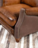 The Cowboy AF Leather Chair is a western-style armchair with a luxurious full-grain leather finish, hand-burnished leather details, and brushed sueded leather accents on the out arms. The chair features plush seat and back cushions, nickel nail trim, and