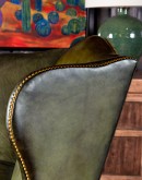American-made Gentry Olive Wingback Chair with hand-brushed olive green leather, gold nail tack detailing, and a sturdy hardwood frame.