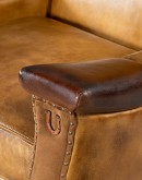 A luxurious Lucky Leather Chair featuring a rich tan full-grain leather upholstery, contrasting leather accents on the arms, brass nail tacks, and a unique leather horseshoe detail.