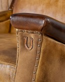 A luxurious Lucky Leather Chair featuring a rich tan full-grain leather upholstery, contrasting leather accents on the arms, brass nail tacks, and a unique leather horseshoe detail.