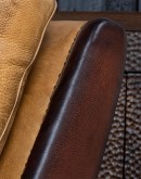 A luxurious Lucky Leather Chair featuring a rich tan full-grain leather upholstery, contrasting leather accents on the arms, brass nail tacks, and a unique leather horseshoe detail.