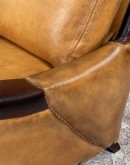 A luxurious Lucky Leather Chair featuring a rich tan full-grain leather upholstery, contrasting leather accents on the arms, brass nail tacks, and a unique leather horseshoe detail.