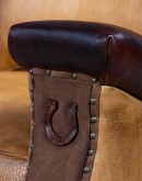 A luxurious Lucky Leather Chair featuring a rich tan full-grain leather upholstery, contrasting leather accents on the arms, brass nail tacks, and a unique leather horseshoe detail.