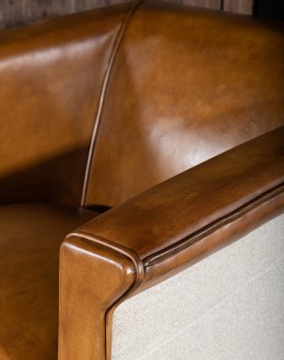 Image of the American-made Polo Club Chair showcasing its full grain leather upholstery with hand burnished details, and luxurious cream nylon tweed-textured fabric wrapping the outside arms and back, signifying modern rustic elegance