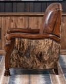 A brown leather recliner chair with a wooden base and armrests is pictured against a plain beige background. The chair has a tight back with a boot stitch emblem and is adorned with premium upholstery grade brindle cowhide on the sides and outside back. T