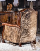 A brown leather recliner chair with a wooden base and armrests is pictured against a plain beige background. The chair has a tight back with a boot stitch emblem and is adorned with premium upholstery grade brindle cowhide on the sides and outside back. T