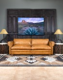 A luxurious tan leather sofa with hand-painted horses and canyon scenes by artist Wayne Parmenter, featuring classic cowboy boot stitching and channel design on the arms, part of Adobe Interiors' Desert Ranch and Mountain Ranch Collection.