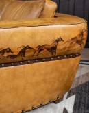 A luxurious tan leather sofa with hand-painted horses and canyon scenes by artist Wayne Parmenter, featuring classic cowboy boot stitching and channel design on the arms, part of Adobe Interiors' Desert Ranch and Mountain Ranch Collection.