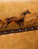 A luxurious tan leather sofa with hand-painted horses and canyon scenes by artist Wayne Parmenter, featuring classic cowboy boot stitching and channel design on the arms, part of Adobe Interiors' Desert Ranch and Mountain Ranch Collection.