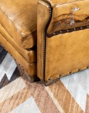 A luxurious tan leather sofa with hand-painted horses and canyon scenes by artist Wayne Parmenter, featuring classic cowboy boot stitching and channel design on the arms, part of Adobe Interiors' Desert Ranch and Mountain Ranch Collection.