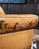 A luxurious tan leather sofa with hand-painted horses and canyon scenes by artist Wayne Parmenter, featuring classic cowboy boot stitching and channel design on the arms, part of Adobe Interiors' Desert Ranch and Mountain Ranch Collection.