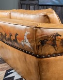 A luxurious tan leather sofa with hand-painted horses and canyon scenes by artist Wayne Parmenter, featuring classic cowboy boot stitching and channel design on the arms, part of Adobe Interiors' Desert Ranch and Mountain Ranch Collection.