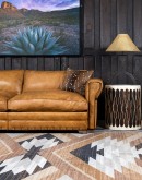 A luxurious tan leather sofa with hand-painted horses and canyon scenes by artist Wayne Parmenter, featuring classic cowboy boot stitching and channel design on the arms, part of Adobe Interiors' Desert Ranch and Mountain Ranch Collection.