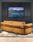 A luxurious tan leather sofa with hand-painted horses and canyon scenes by artist Wayne Parmenter, featuring classic cowboy boot stitching and channel design on the arms, part of Adobe Interiors' Desert Ranch and Mountain Ranch Collection.