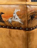 A luxurious tan leather sofa with hand-painted horses and canyon scenes by artist Wayne Parmenter, featuring classic cowboy boot stitching and channel design on the arms, part of Adobe Interiors' Desert Ranch and Mountain Ranch Collection.