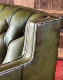 An image of the Ellis Swivel Chair, crafted in the USA with a boxy silhouette, track arms, and deep button-tufted seat back. Upholstered in olive green full-grain leather with hand-burnished details and nickel nail head trim along the arm rails and upper 