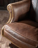True Grit Executive Desk Chair in full-grain brown leather with gold-finish brass nail tacks and leather suede sides, showcasing ergonomic wingback design for superior comfort.