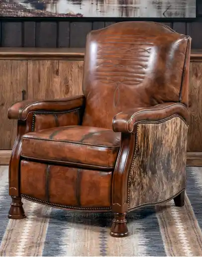 A brown leather recliner chair with a wooden base and armrests is pictured against a plain beige background. The chair has a tight back with a boot stitch emblem and is adorned with premium upholstery grade brindle cowhide on the sides and outside back. T